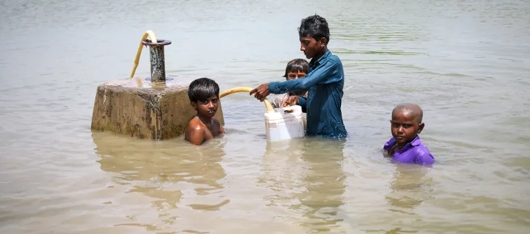 Jongens wagen zich in het overstromingswater om hun jerrycans te vullen met drinkwater in Sindh, Pakistan. - © UNICEF/UN0701707/Zaidi